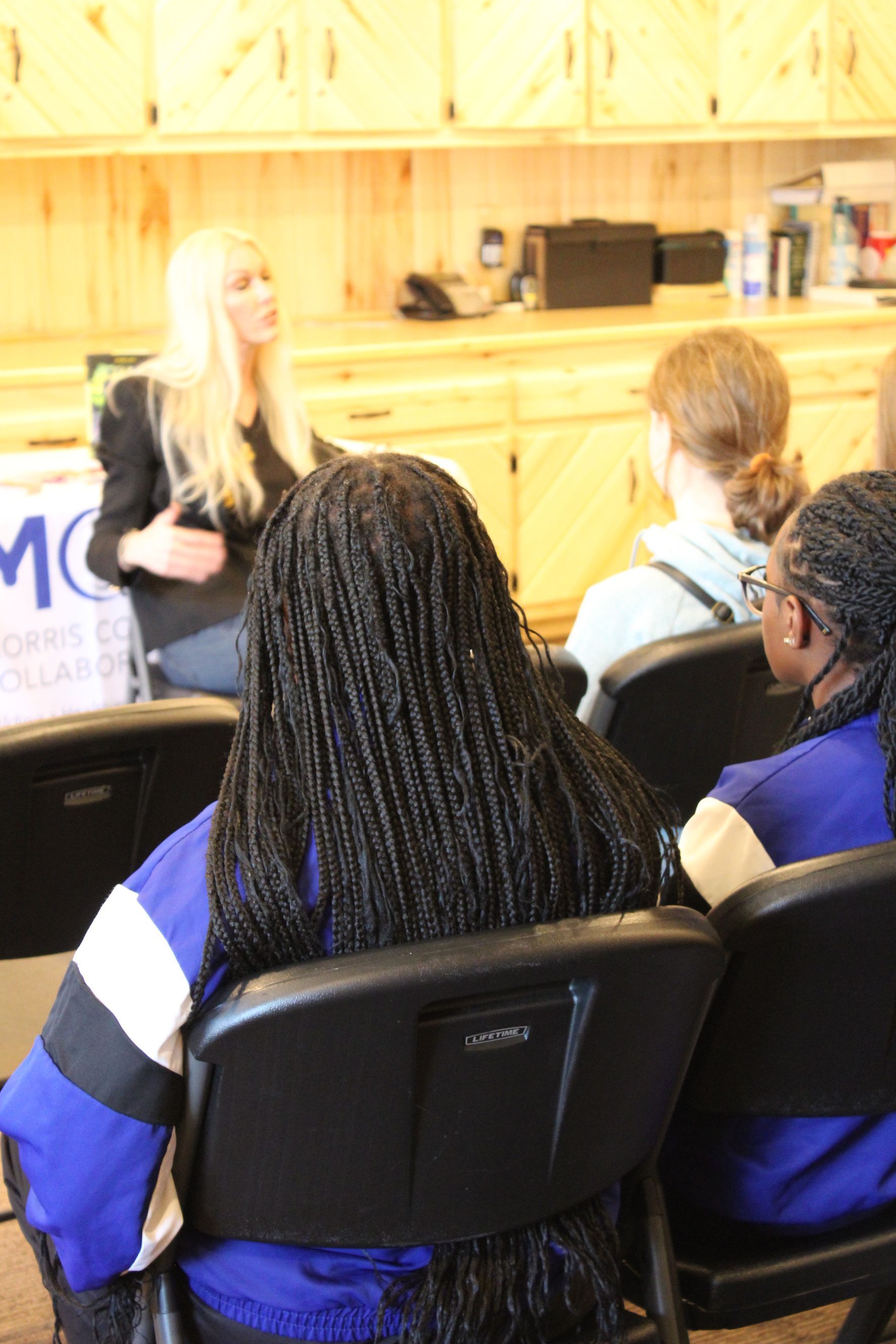 A group of people are sitting in chairs in front of a sign that says mc
