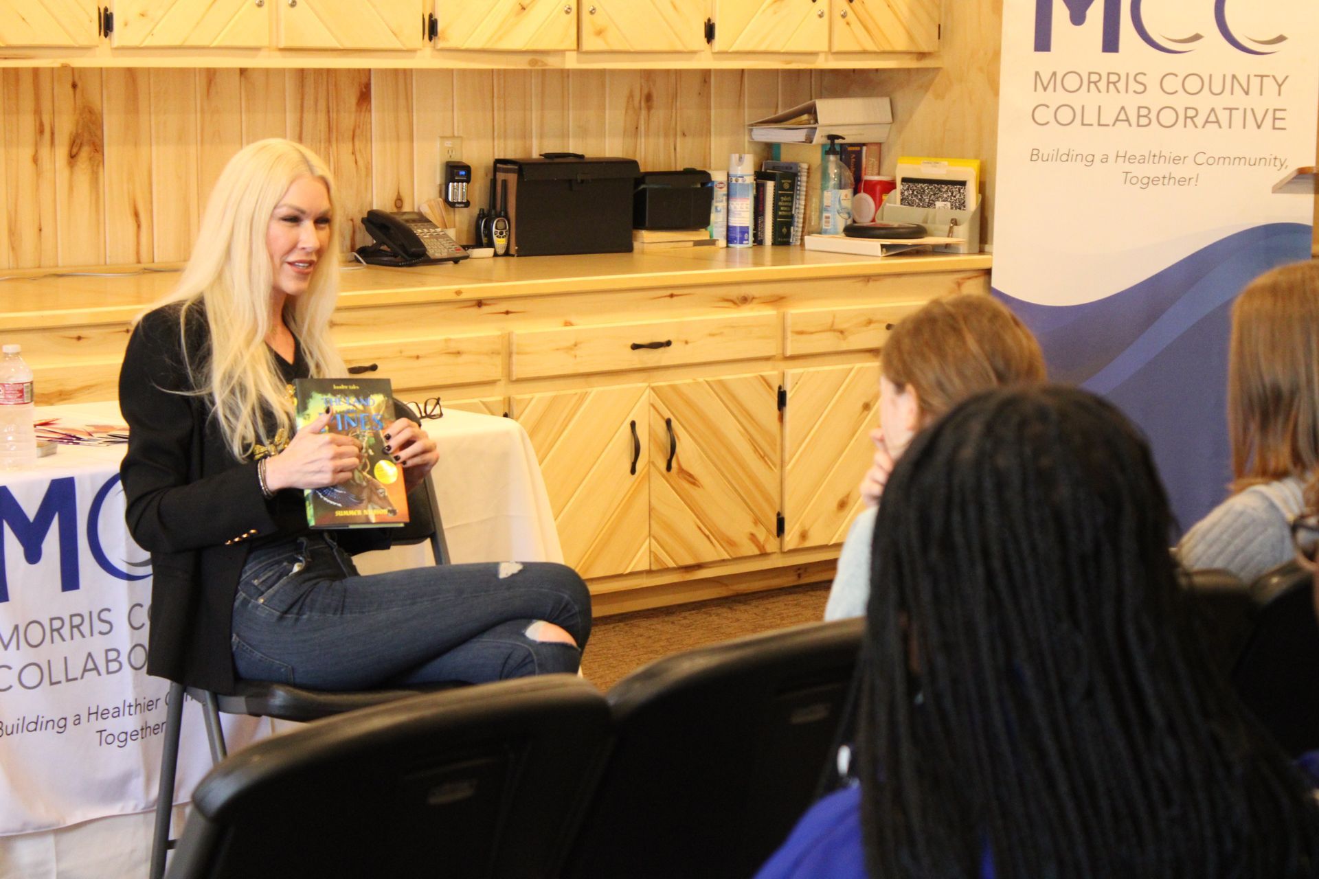 A woman is sitting in a chair reading a book to a group of people.