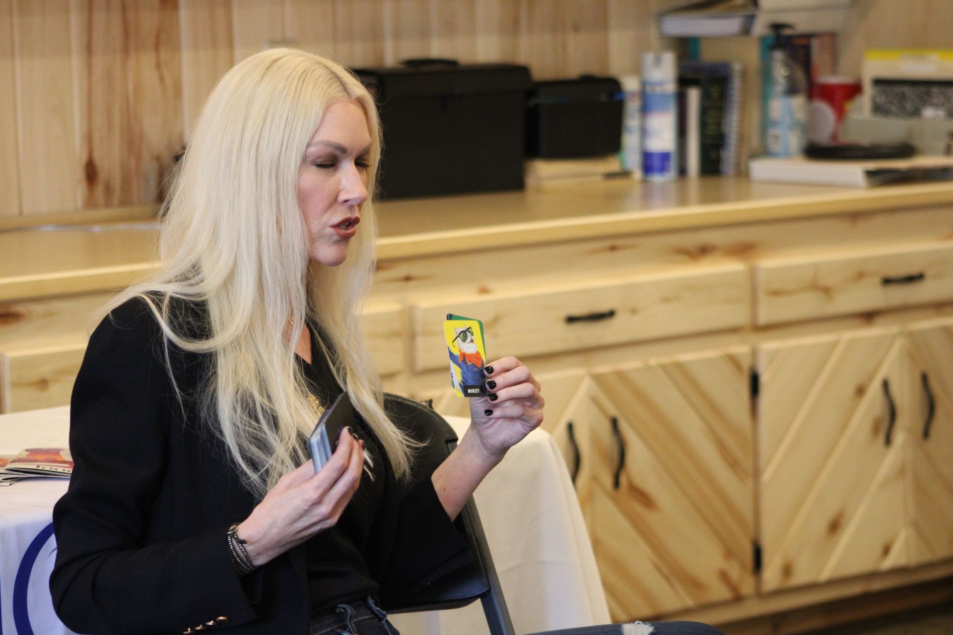 A woman is sitting at a table holding a card in her hand.