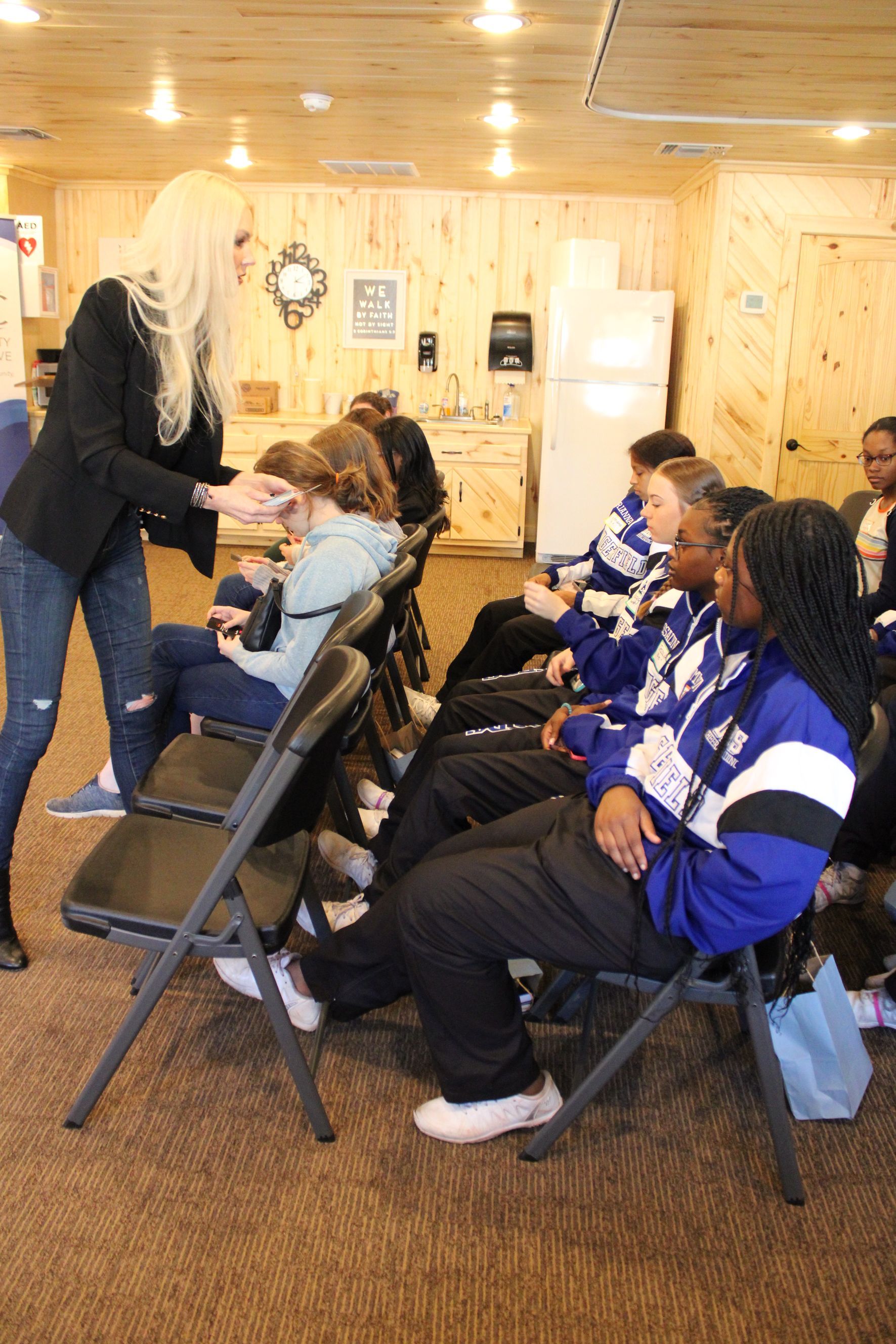 A woman is talking to a group of people sitting in folding chairs