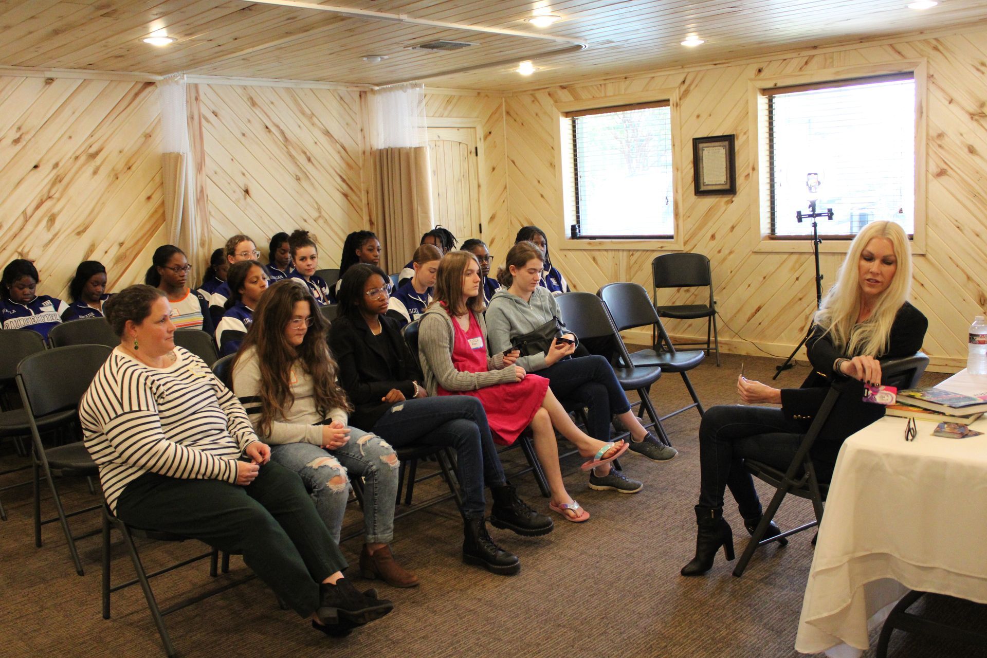 A woman is sitting at a table talking to a group of people sitting in chairs.