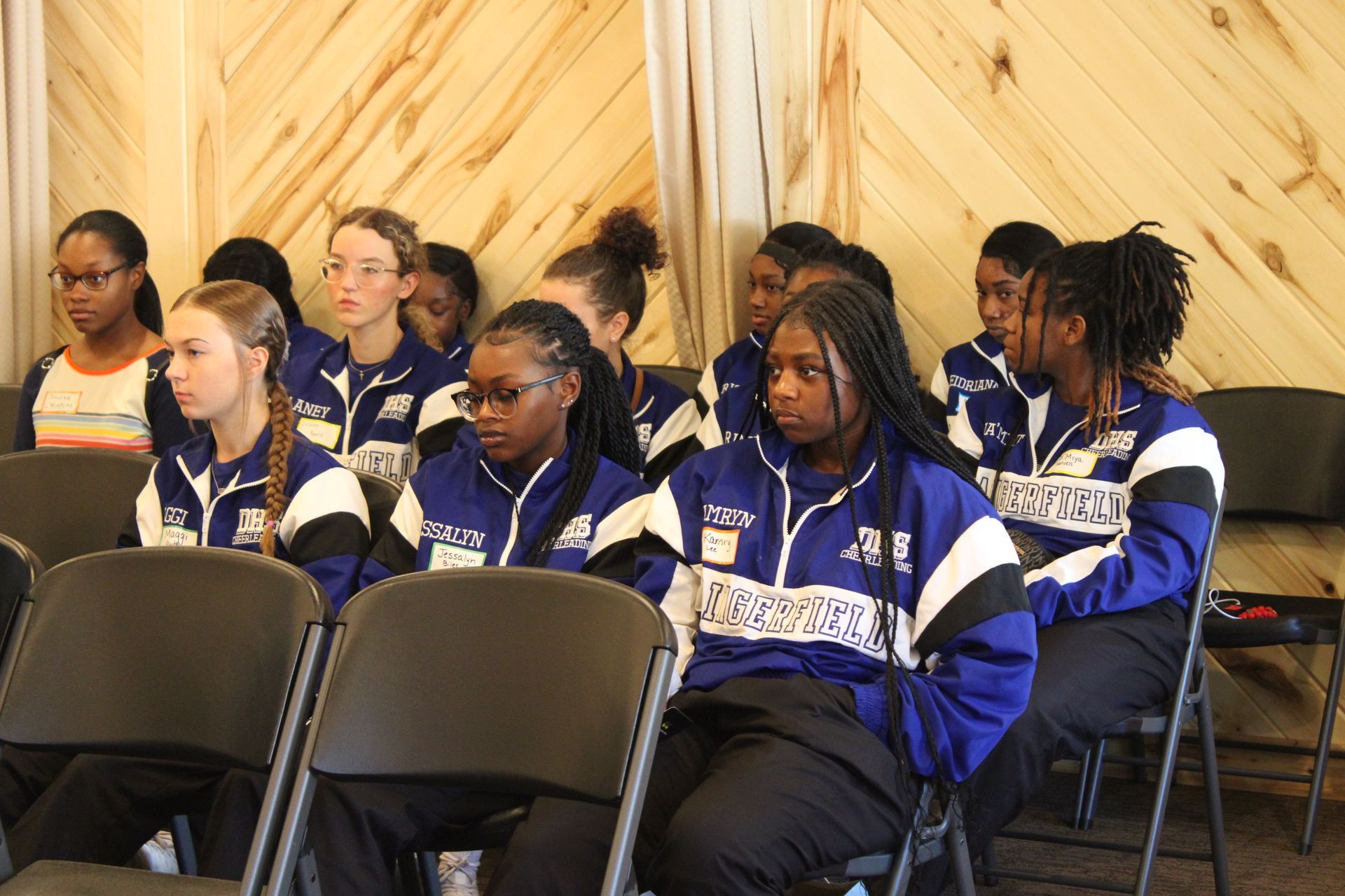 A group of young people are sitting in chairs wearing blue and white jackets