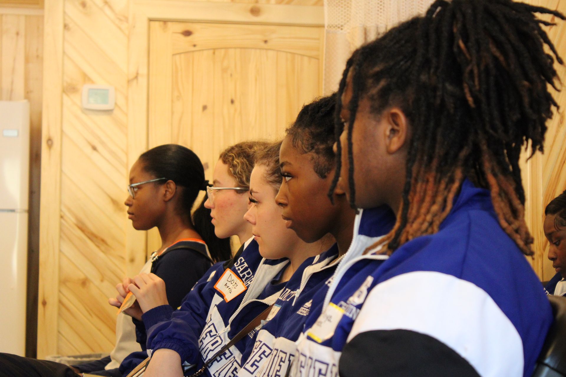 A group of people are sitting in a room and one of them has a name tag that says ' lsu ' on it