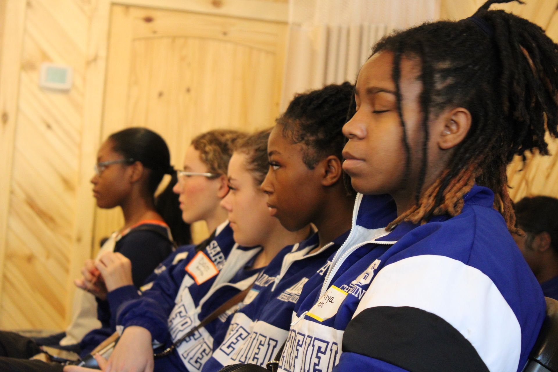 A group of girls are sitting in a row with their eyes closed