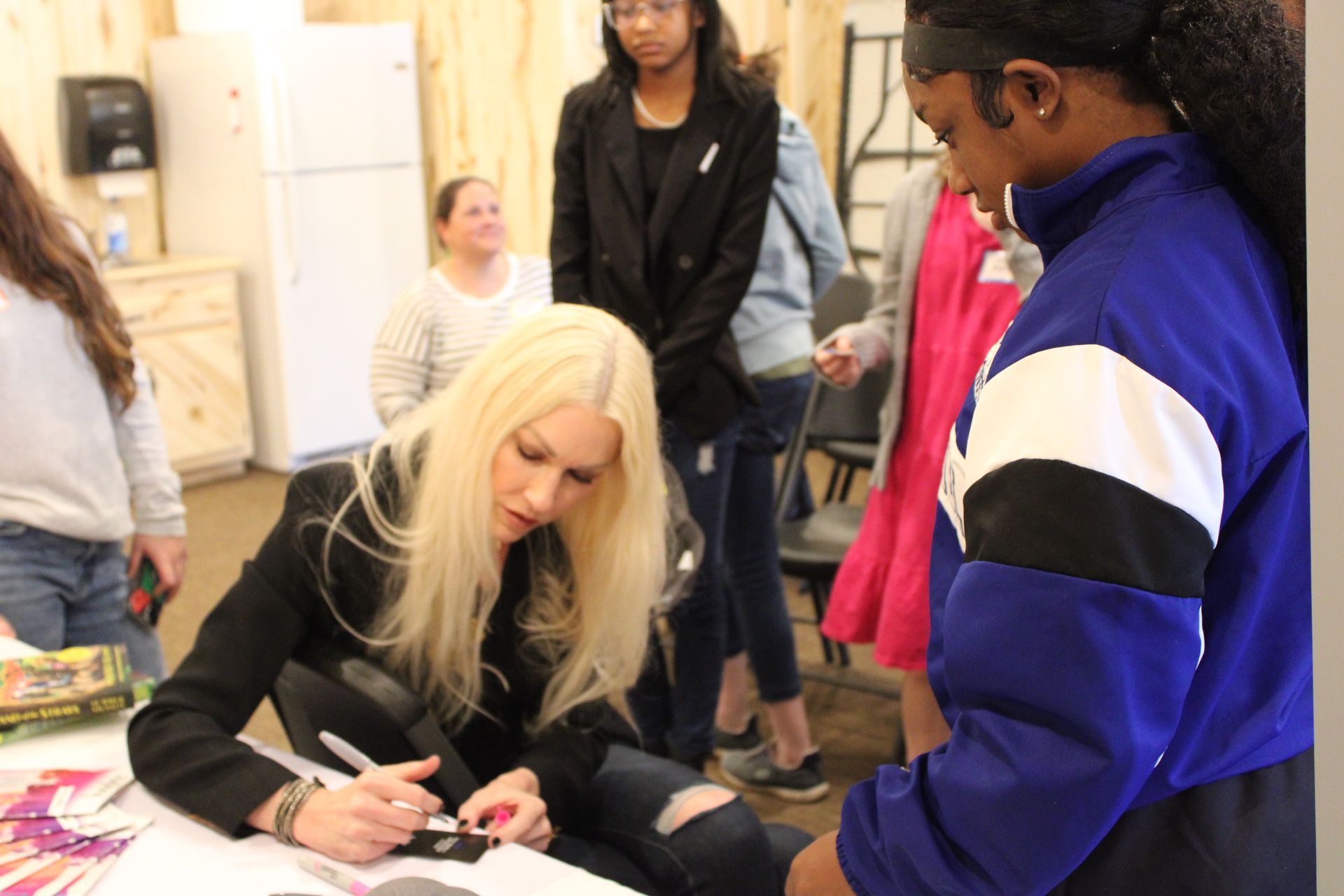 A woman is sitting at a table signing a book for a girl.