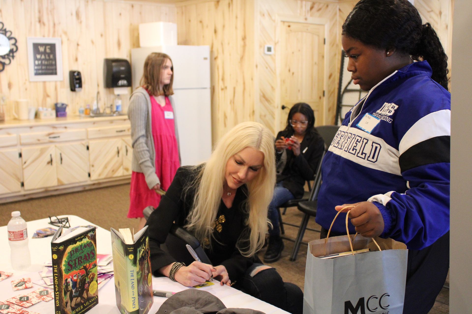 A woman is signing a book for a girl in a room.