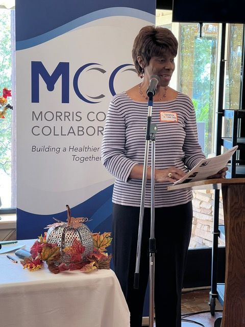 A woman stands at a podium in front of a morris co collaborator banner