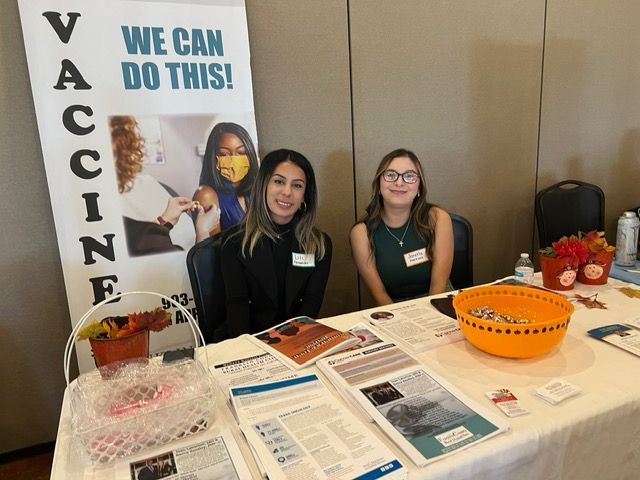 Two women are sitting at a table with a sign that says we can do this