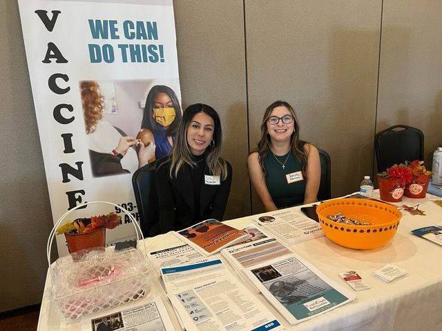 Two women are sitting at a table with a sign that says we can do this.