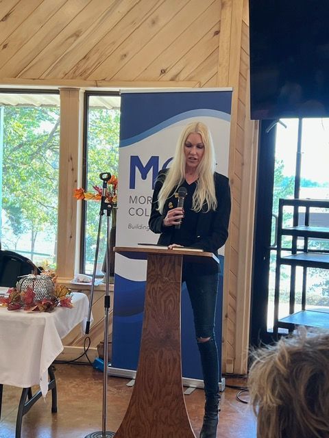 A woman stands at a podium in front of a sign that says mos college