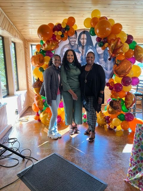 Three women are posing for a picture in front of a balloon arch.