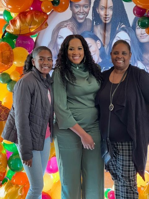 Three women are posing for a picture in front of balloons.