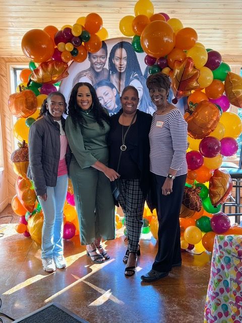 A group of women are posing for a picture in front of a wall of balloons.