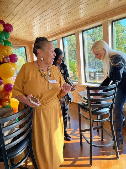 A woman in a yellow dress is talking into a microphone while two other women look on.