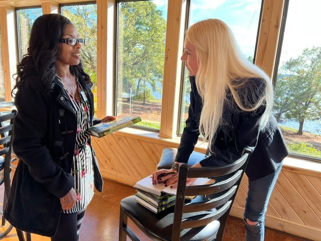 Two women are standing next to each other in front of a window.