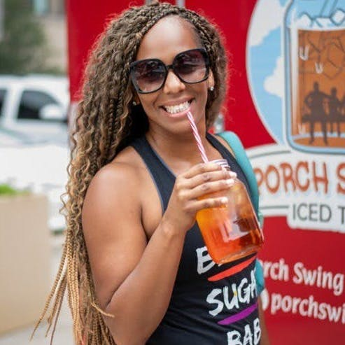 A woman drinking from a bottle with a straw in front of a sign that says porch swing