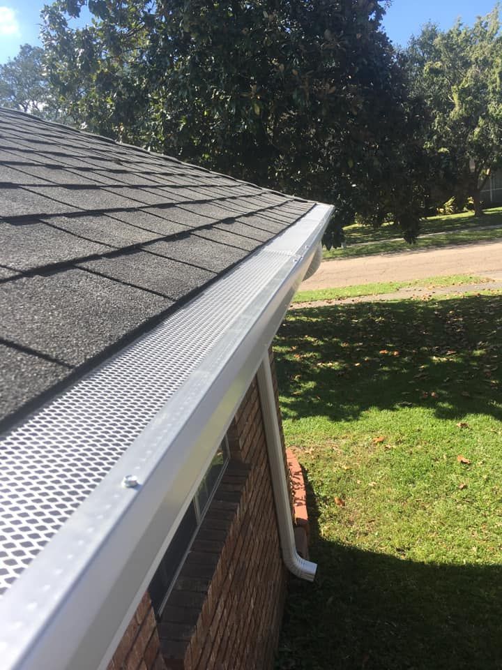 A gutter on the side of a brick house with a tree in the background.
