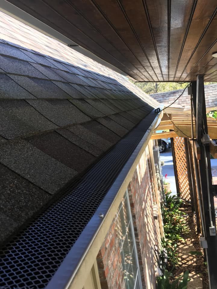 A gutter on the side of a house with a roof in the background.