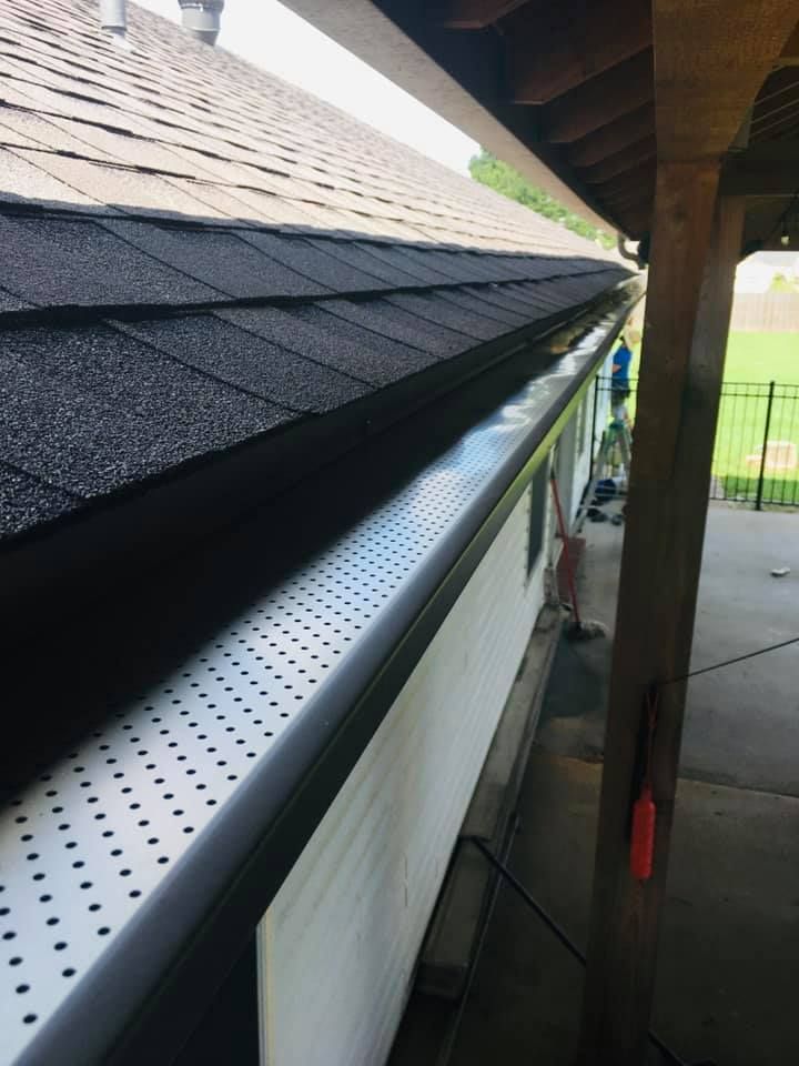 A gutter on the side of a house with a baseball field in the background.