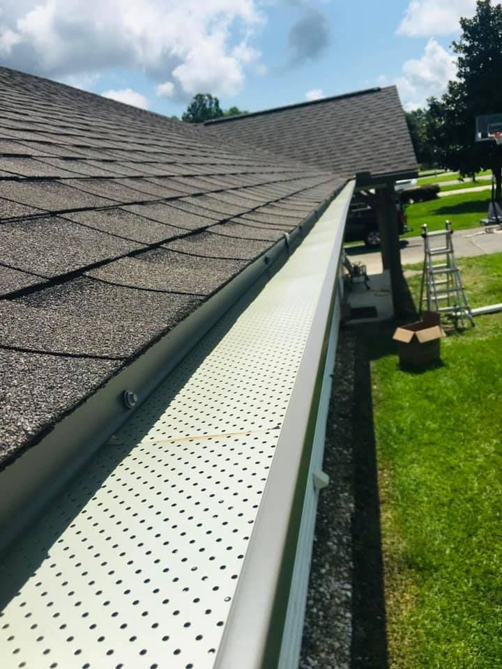 A gutter on the side of a house with a ladder in the background
