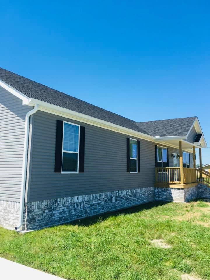 A mobile home with a gray siding and black shutters is sitting on top of a lush green lawn.