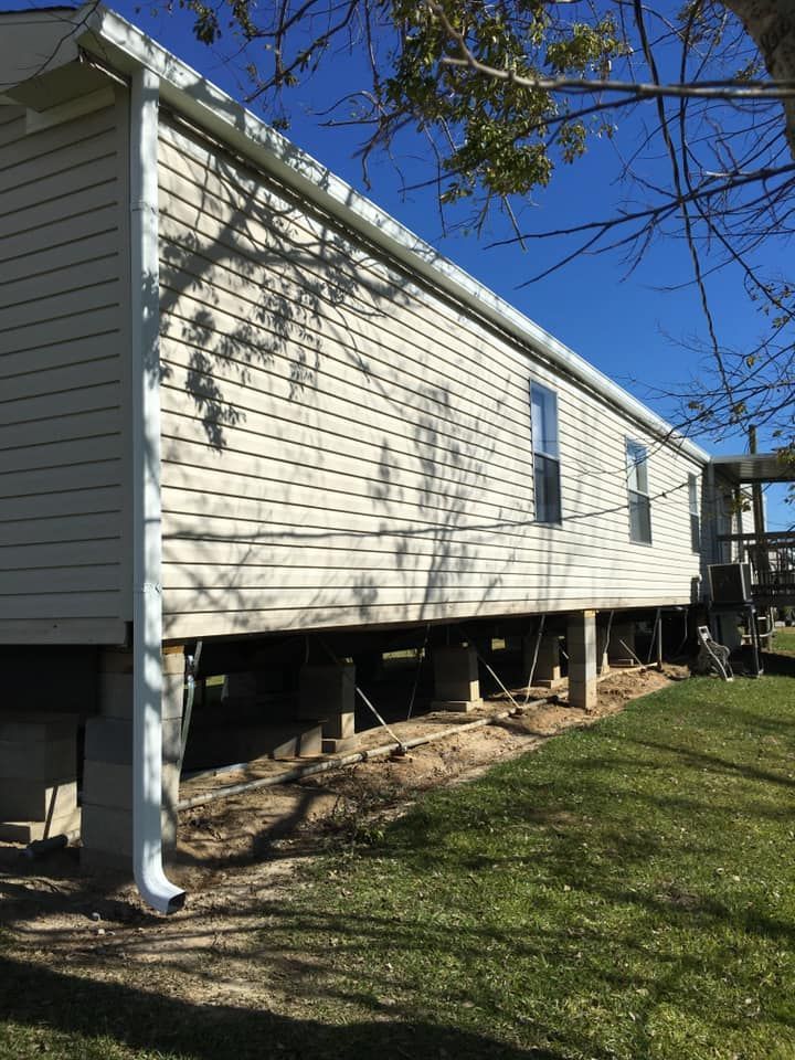 A mobile home is sitting on stilts in a grassy yard.