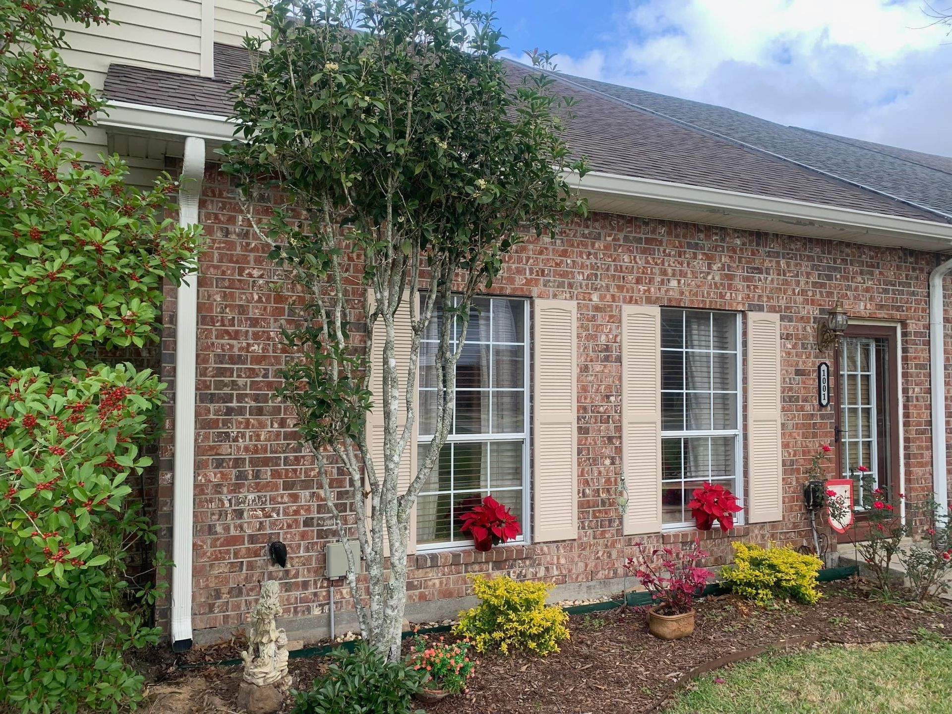 A brick house with white shutters and a tree in front of it