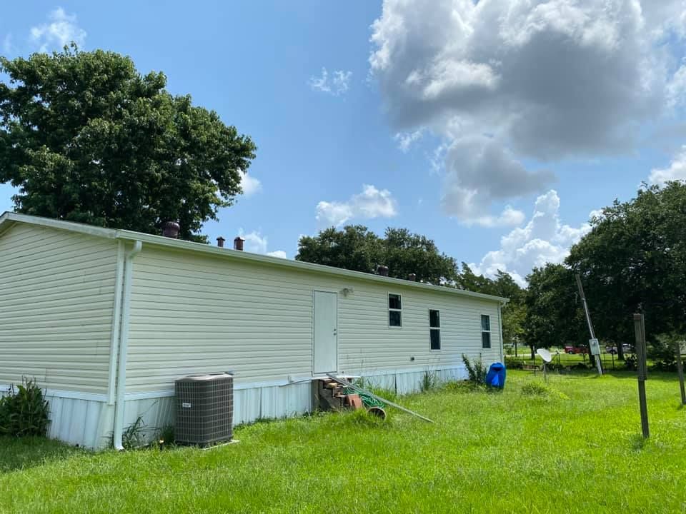 A white mobile home is sitting in the middle of a grassy field.