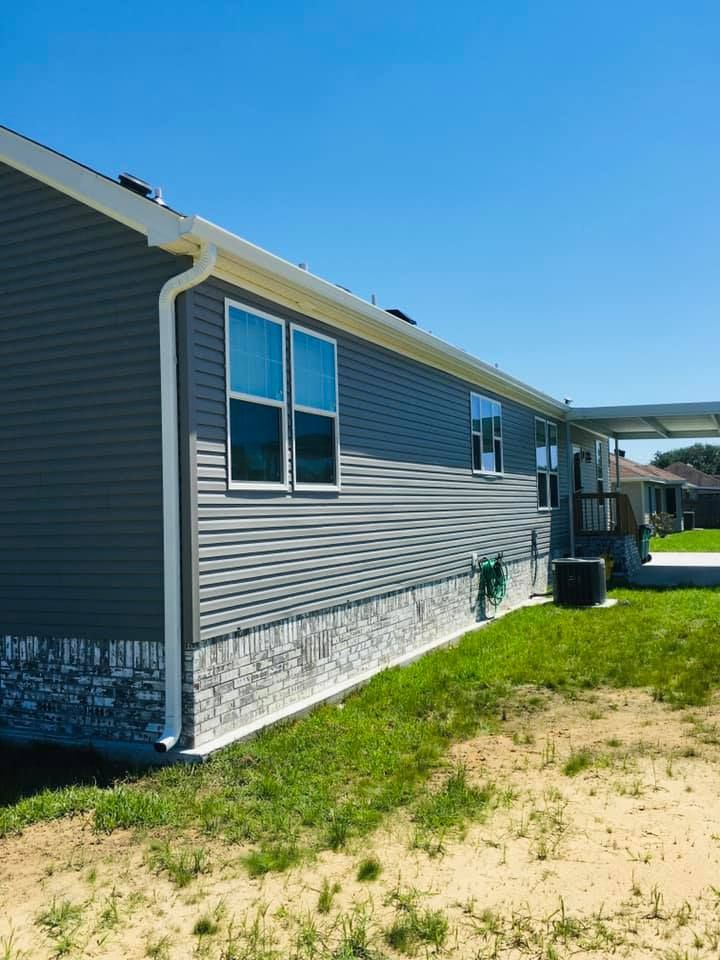 The side of a mobile home with a carport and a lot of windows.