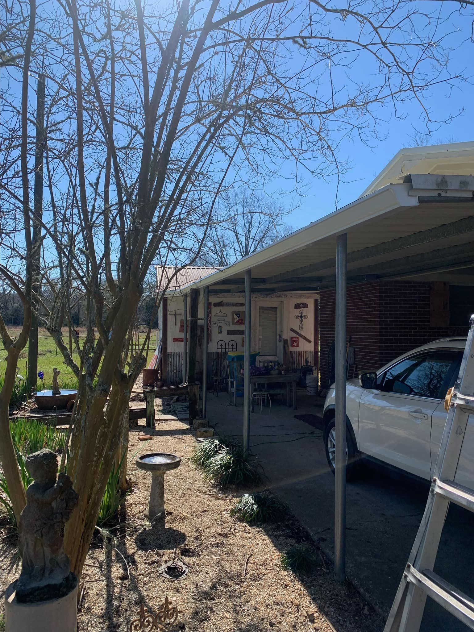 A car is parked under a canopy in front of a house.