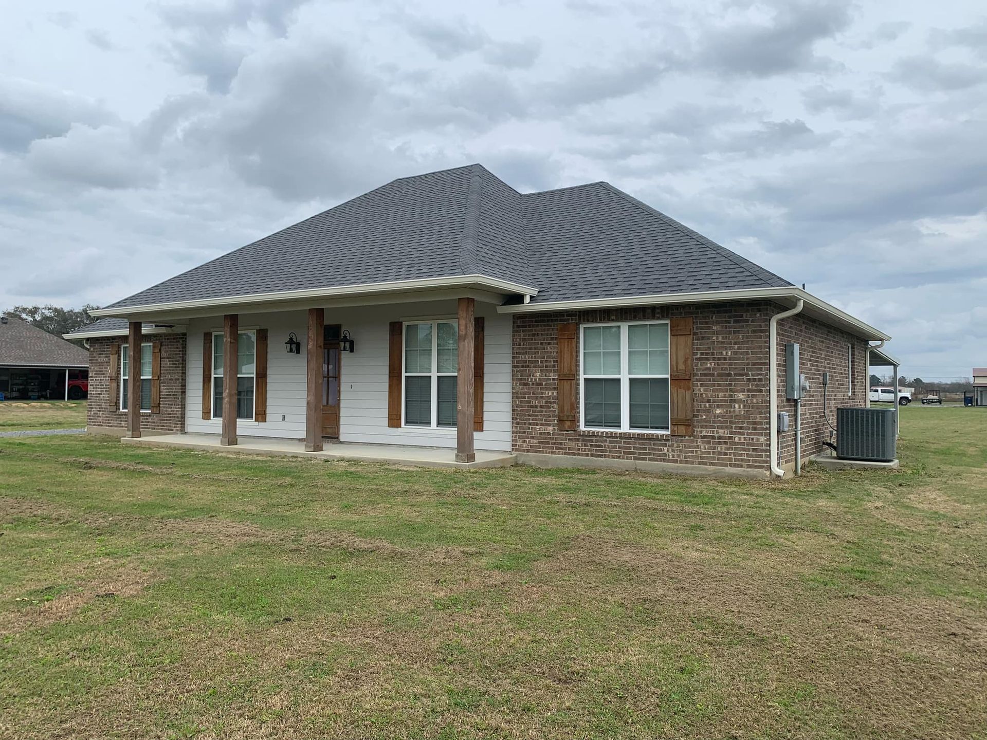 A brick house with a porch and a gray roof is sitting on top of a lush green field.