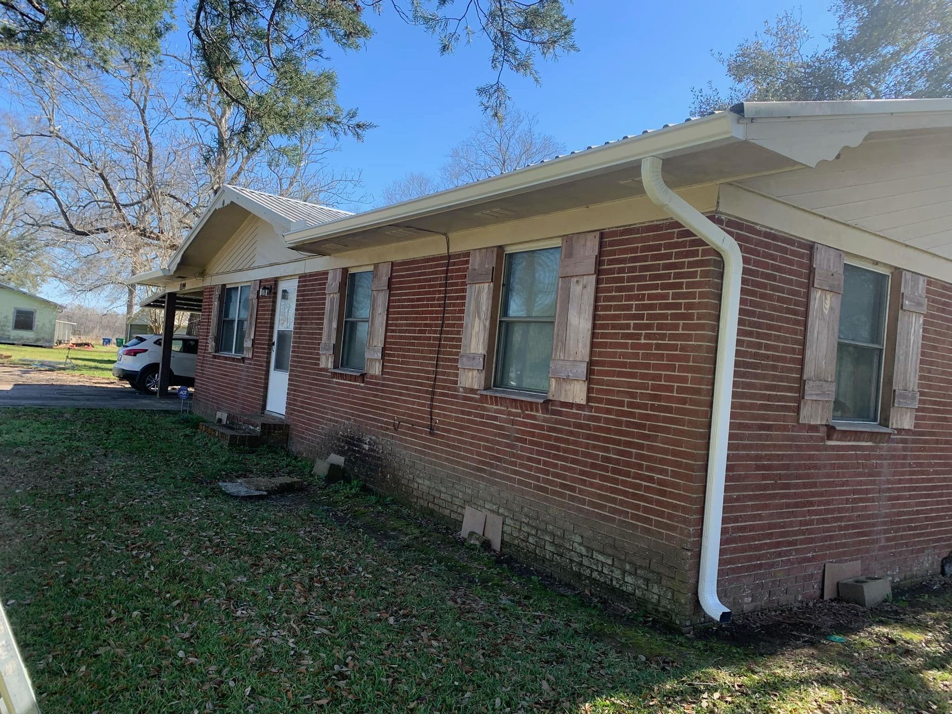 A brick house with a white gutter and shutters on the windows.