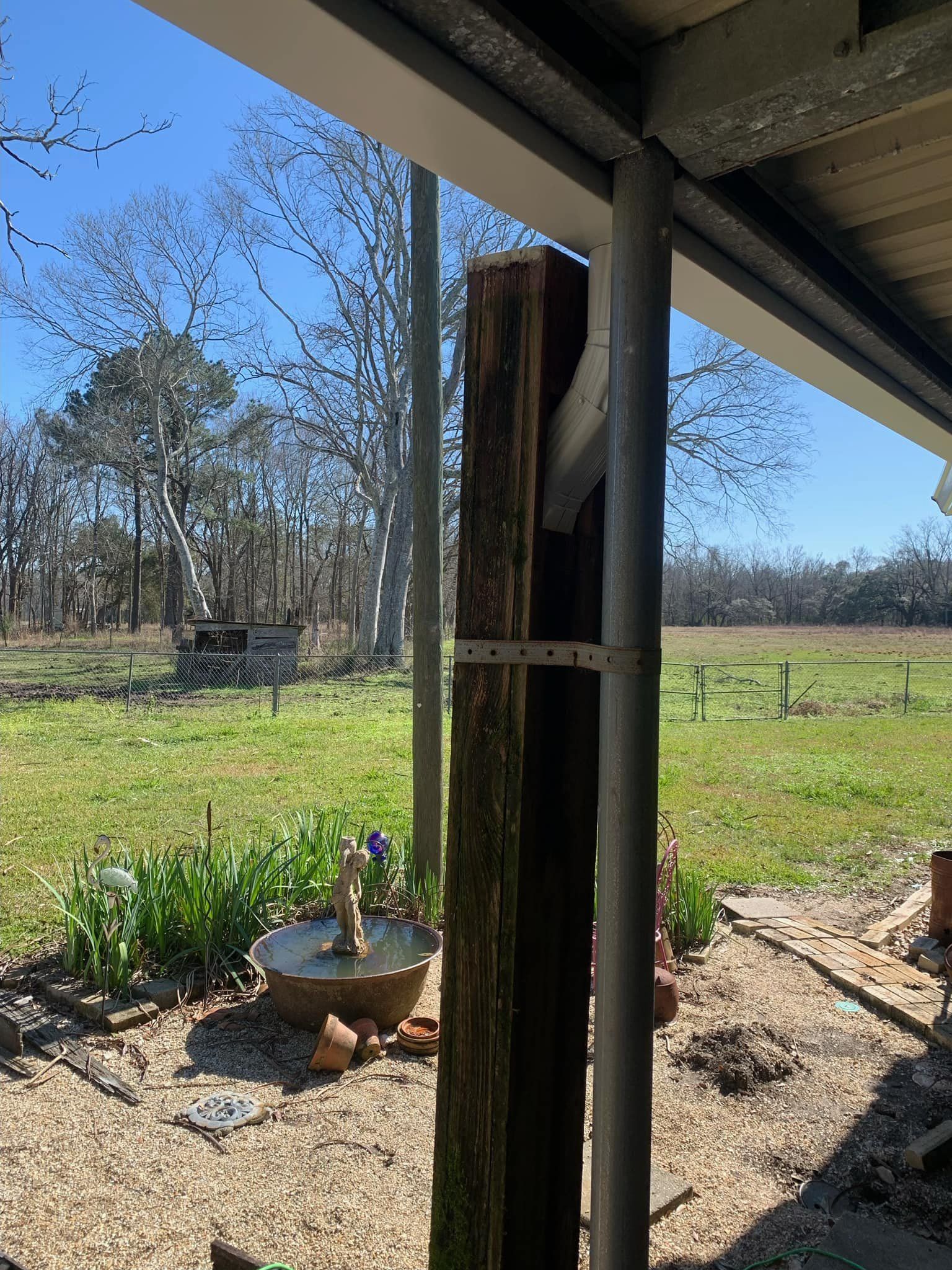 A wooden post is tied to a metal pole in front of a field.