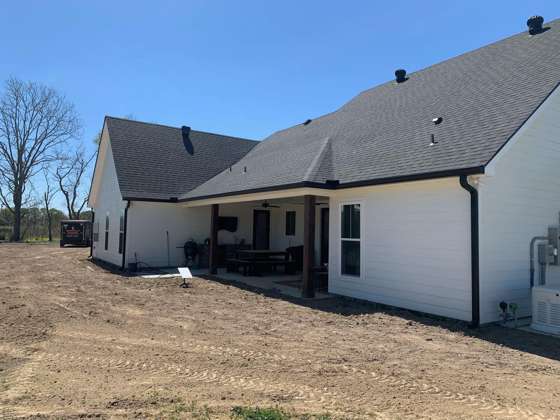 A white house with a gray roof is sitting on top of a dirt field.
