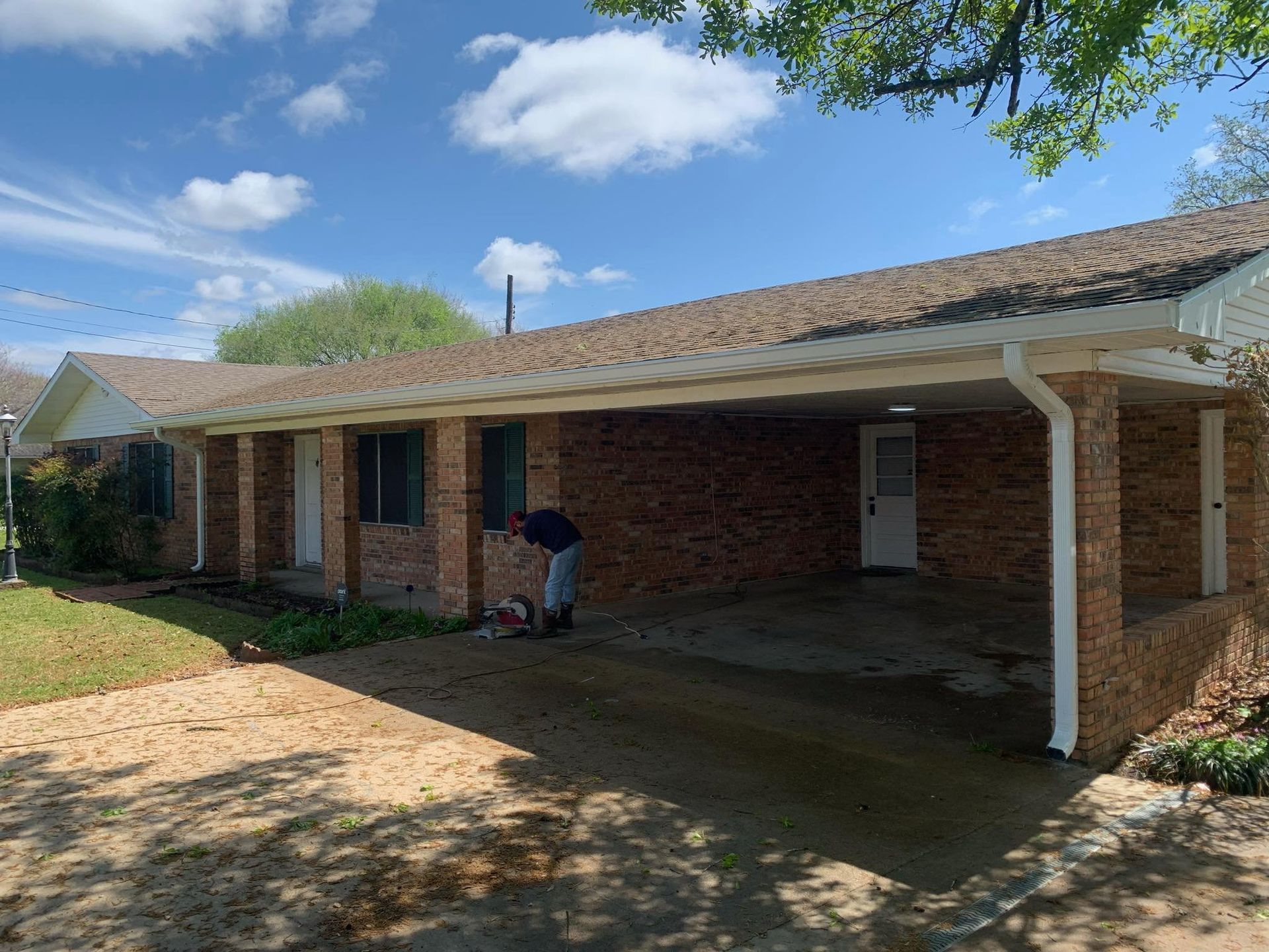 A man is standing in front of a brick house with a carport.