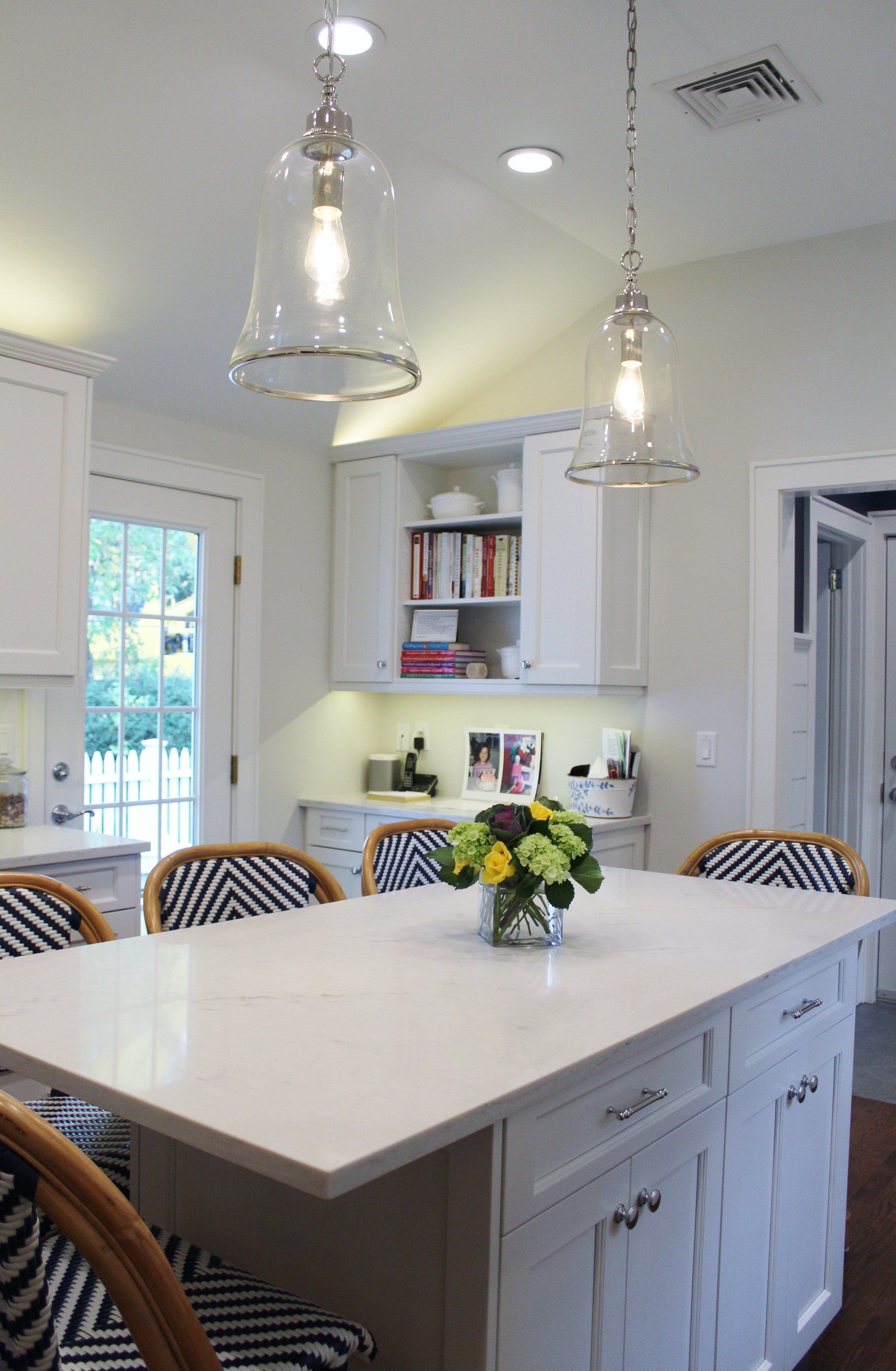A kitchen with white cabinets and a large island with a vase of flowers on it.
