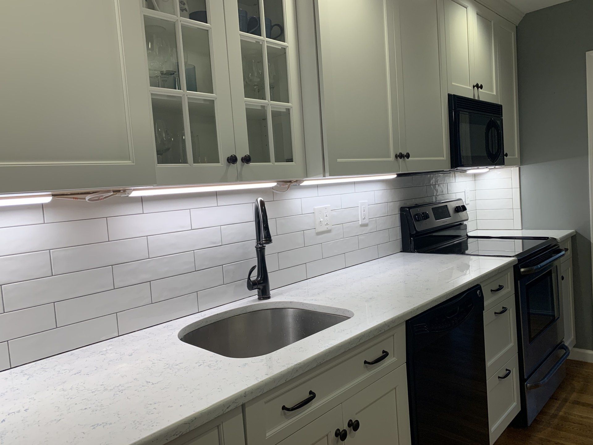A kitchen with white cabinets , a sink , a stove , and a microwave.
