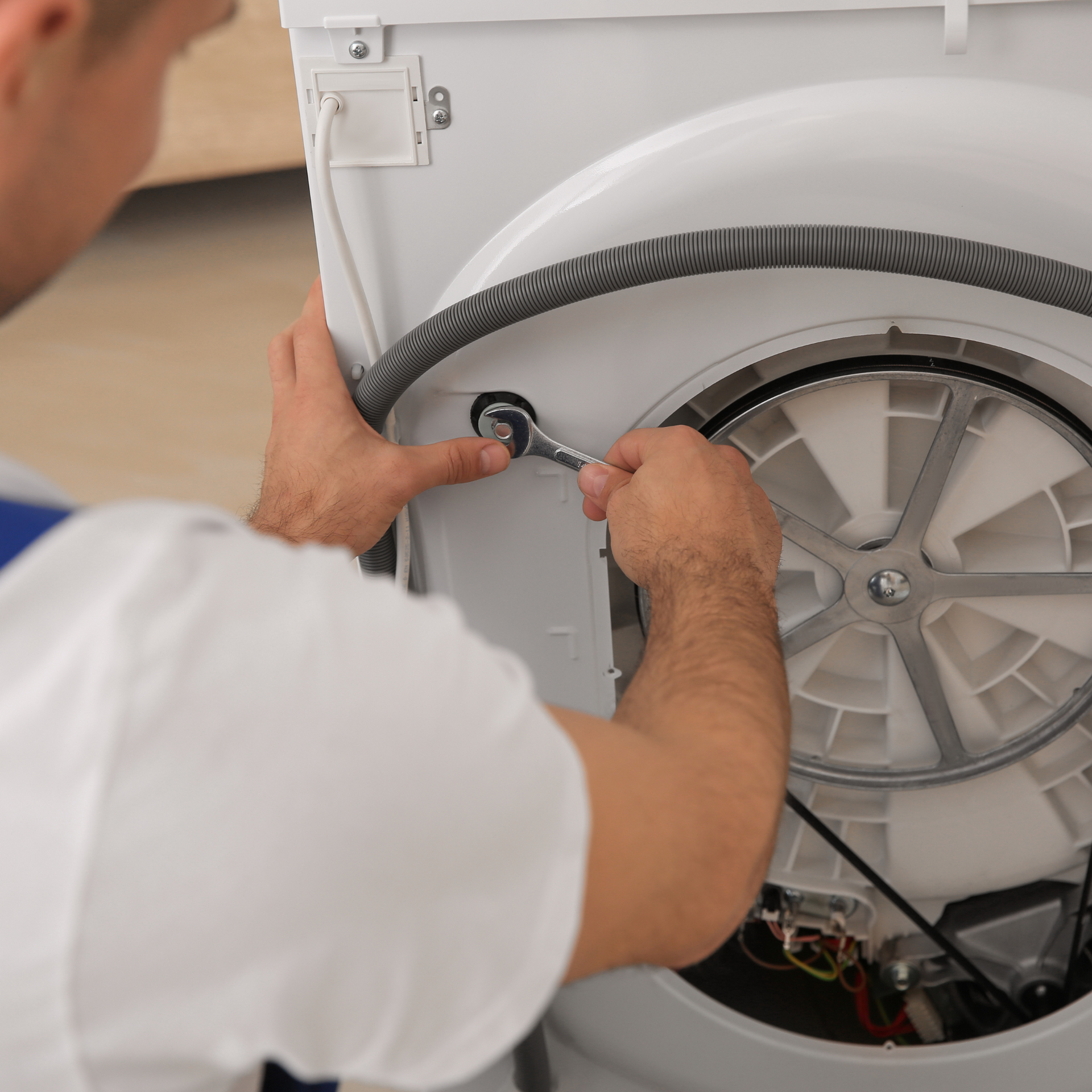 A man is fixing a washing machine with a wrench.