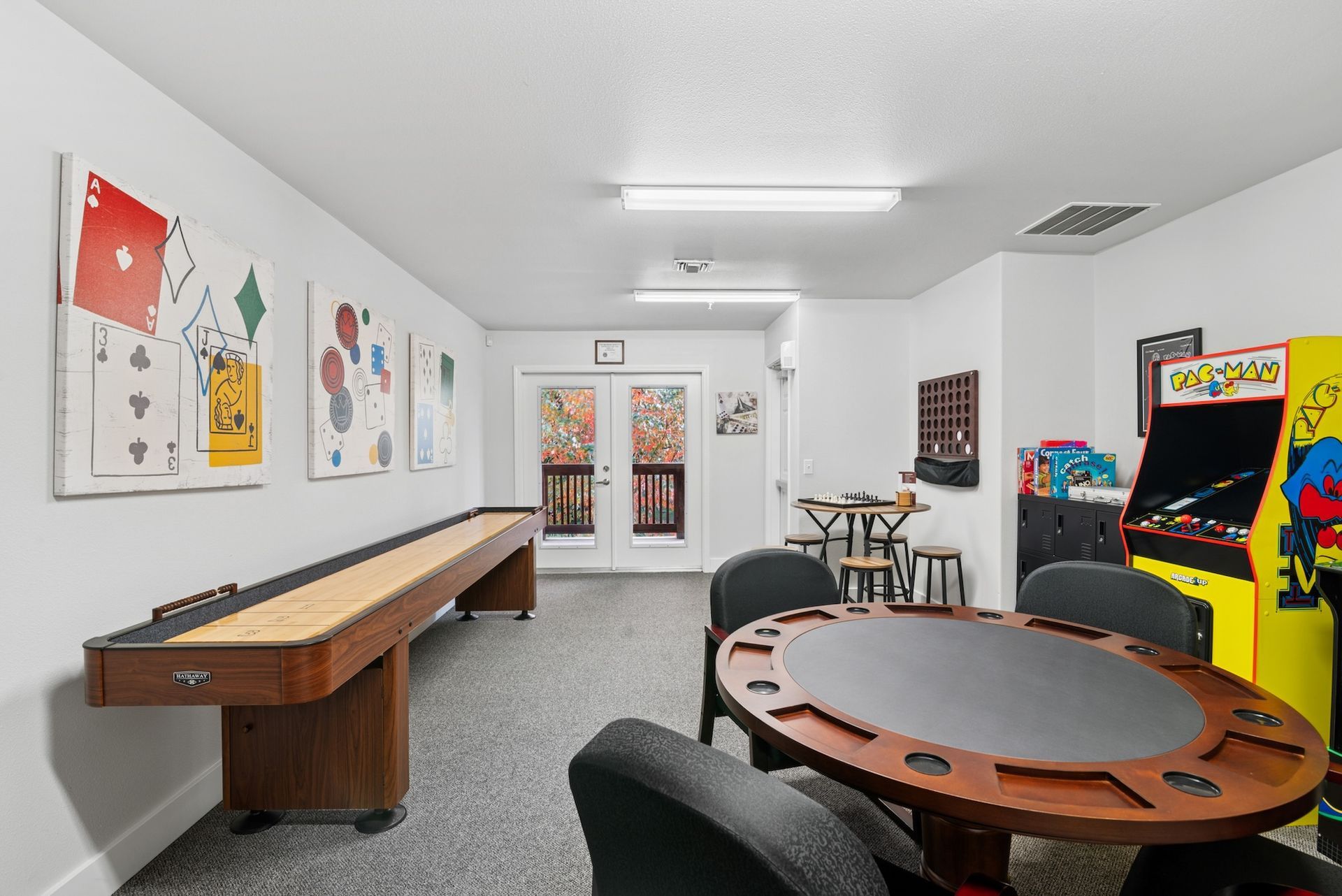 Game room with a shuffleboard, arcade game, card table, and playing card artwork on walls.