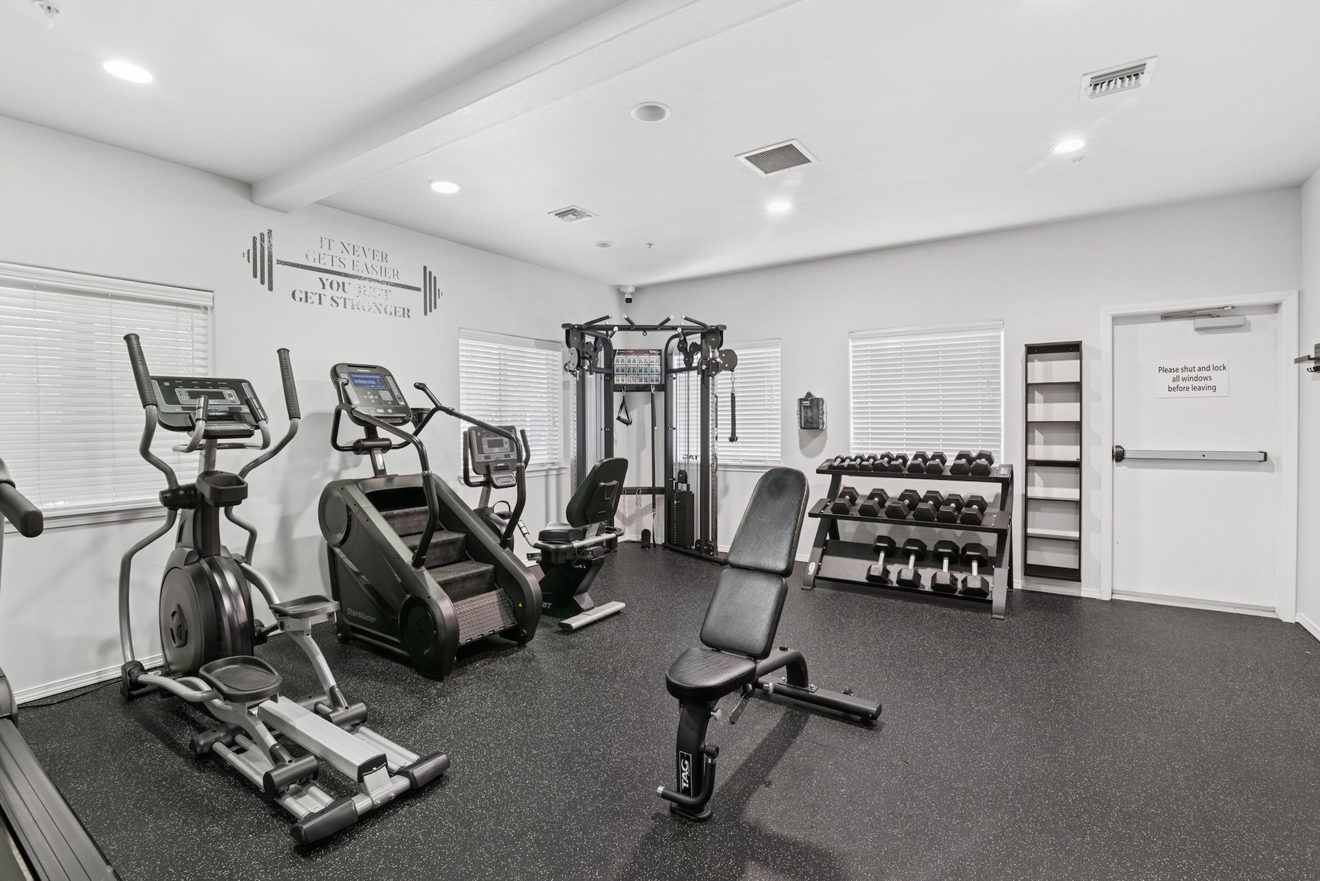 Gym with cardio machines, weights, and a weight bench on a black floor.