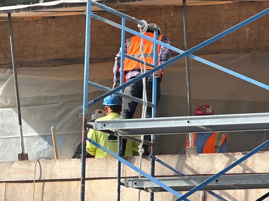 Two construction workers are standing on a scaffolding.