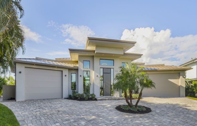 A modern house with a brick driveway and a palm tree in front of it.