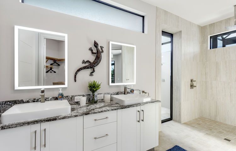 A bathroom with two sinks , two mirrors and a walk in shower.