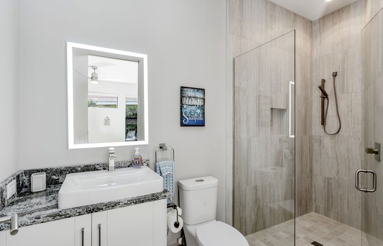 A bathroom with a toilet , sink , mirror and walk in shower.