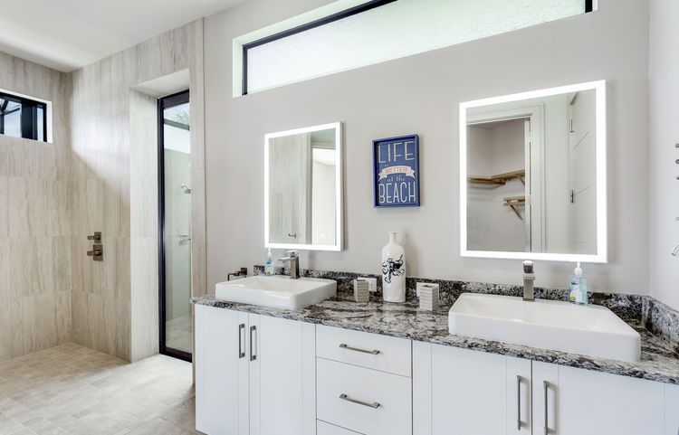 A bathroom with two sinks , two mirrors and a walk in shower.