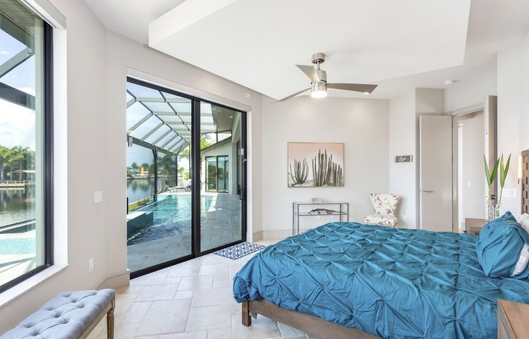 A bedroom with a large bed , sliding glass doors , a ceiling fan and a bench.
