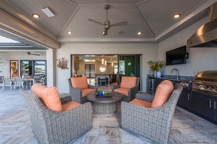 A patio with wicker furniture , a table , chairs and a grill.