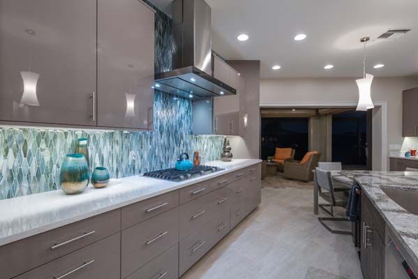 A kitchen with gray cabinets , a stove , a sink , and a stainless steel hood.