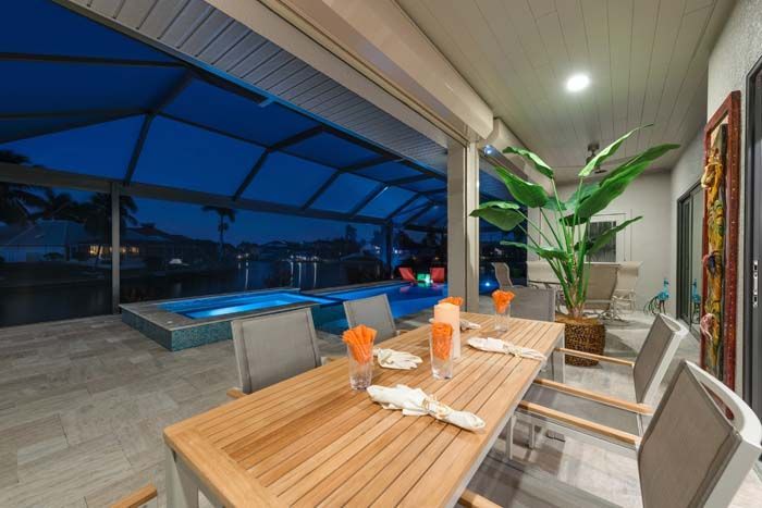 A patio with a table and chairs and a pool at night.