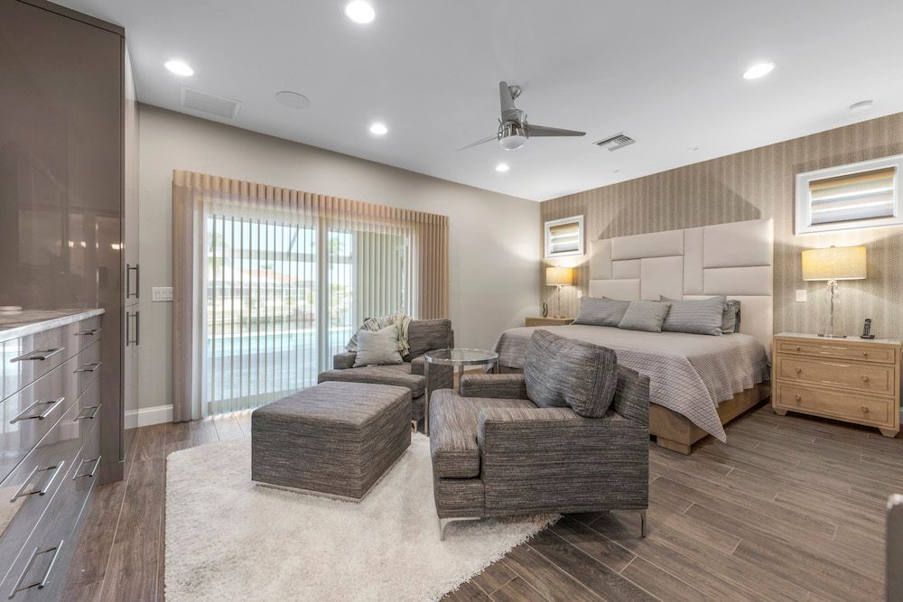 A large bedroom with a king size bed , chairs , ottoman and a ceiling fan.